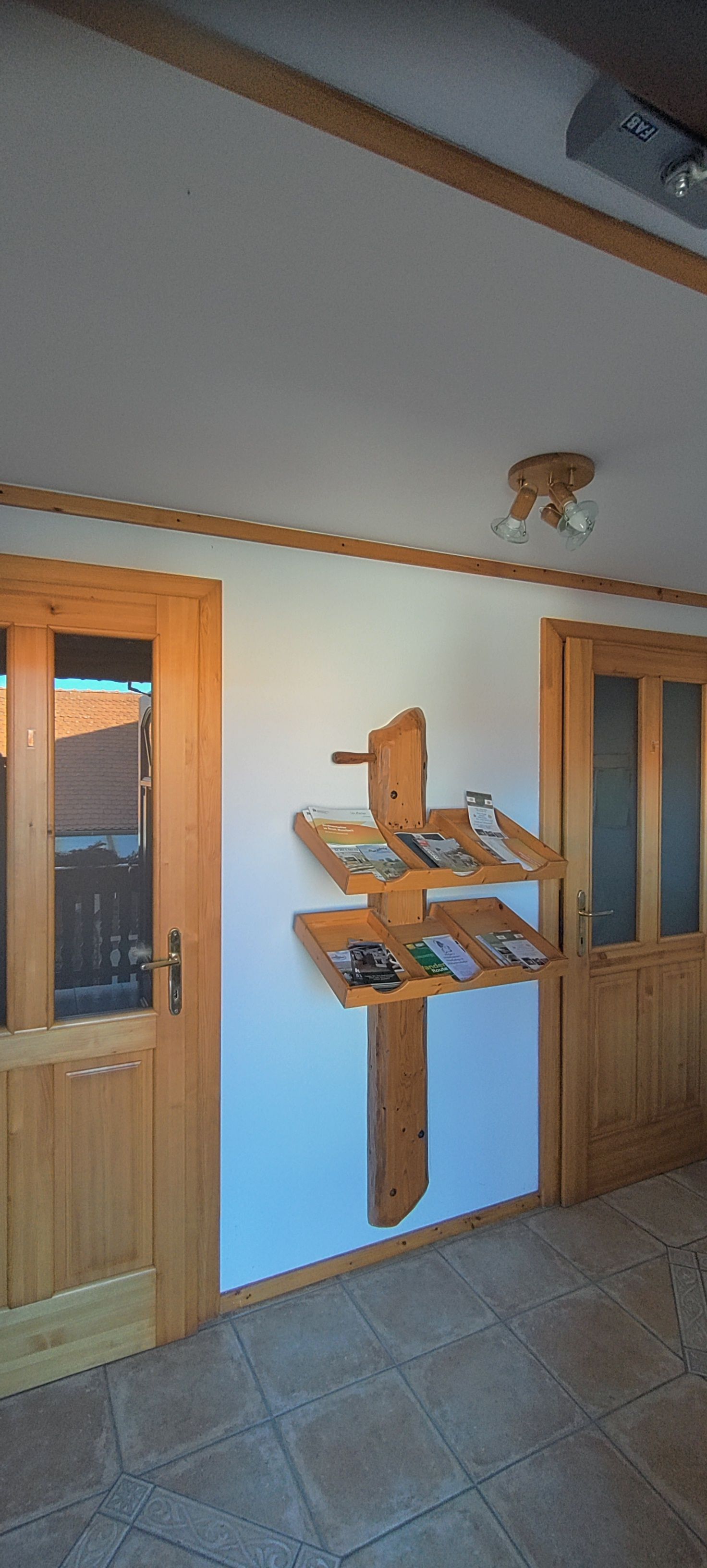 Drevená polica s brožúrami na bielej stene medzi dvoma drevenými dverami.