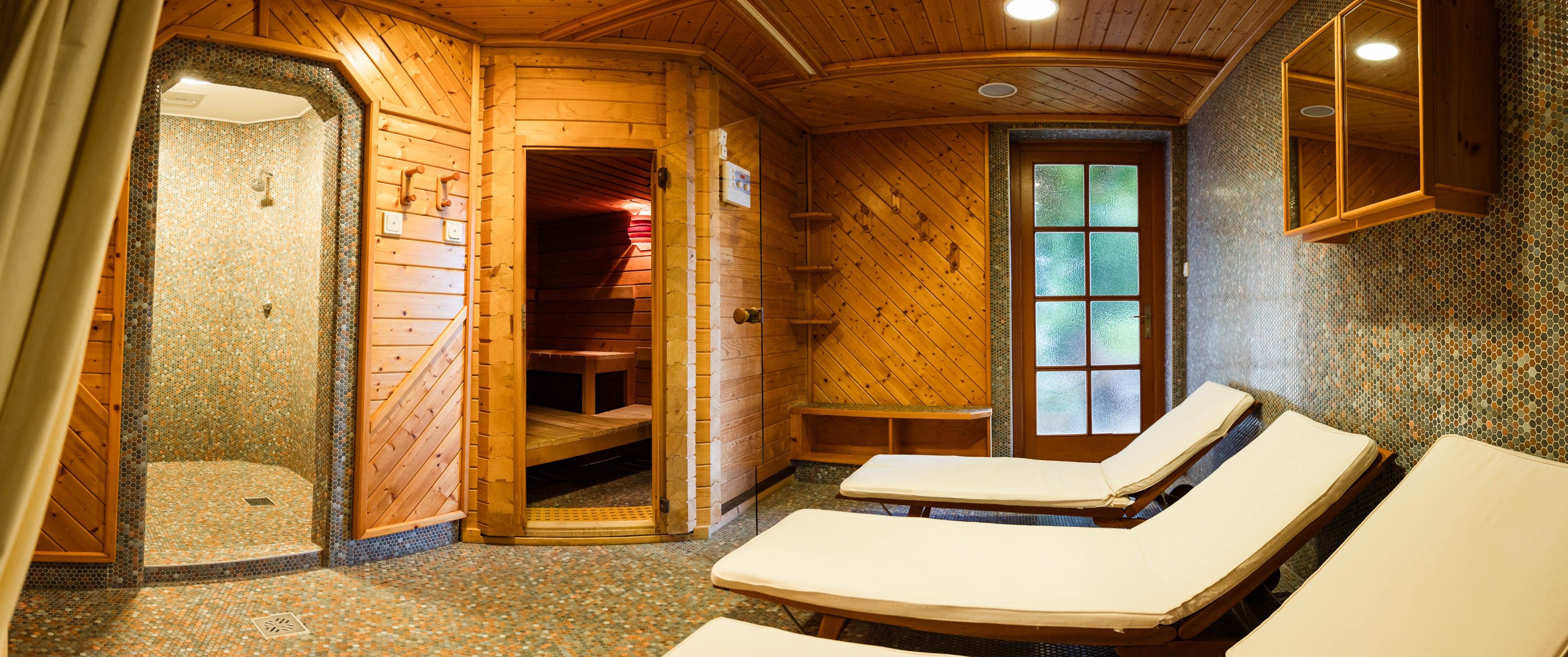 Útulná sauna s dreveným obložením, ležadlami a sprchou.