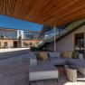 Vnútorný dvor modernej budovy s drevenými prvkami, skleneným zábradlím a sivým sedacím nábytkom.