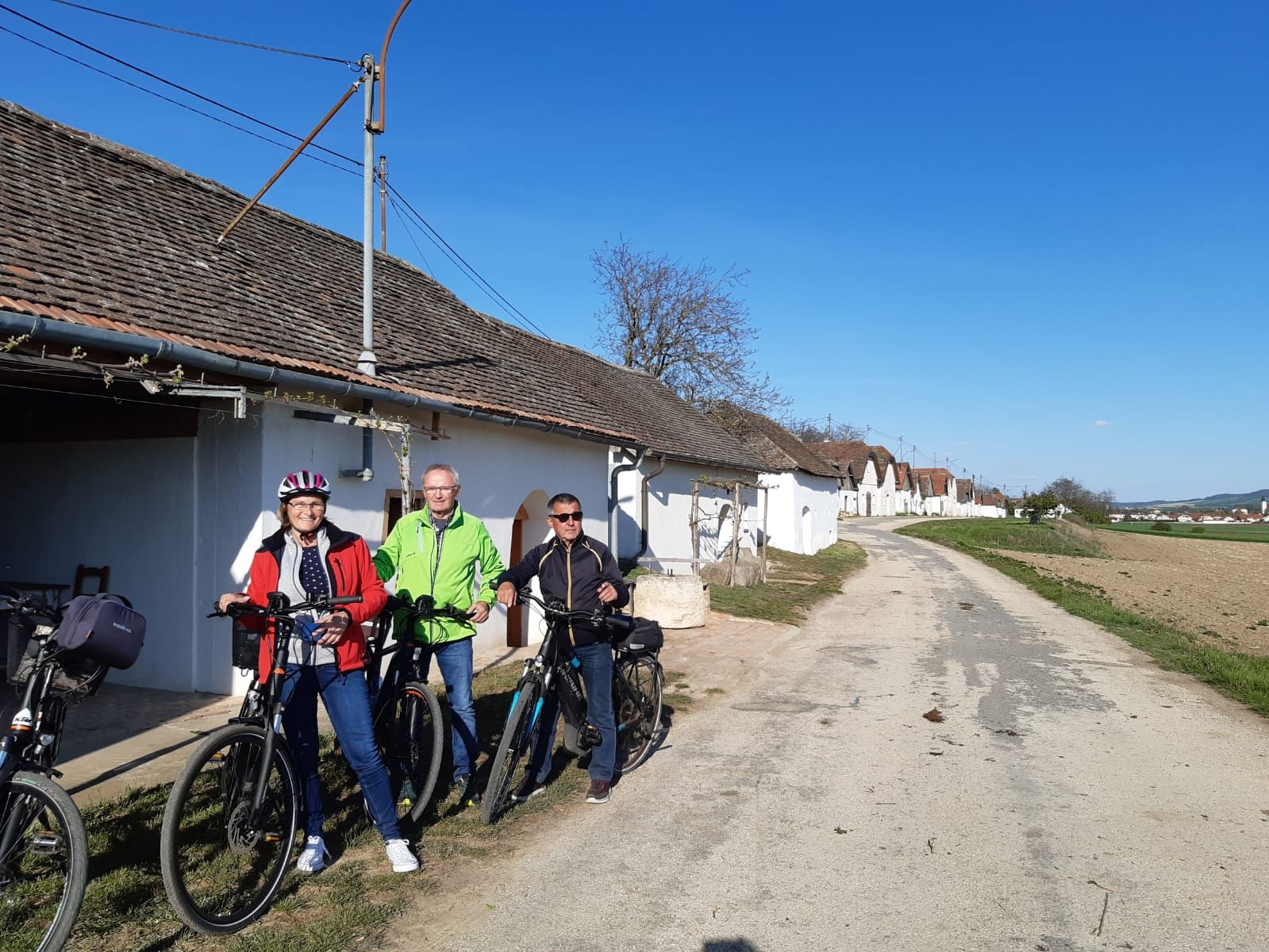 Traja ľudia s bicyklami pred radom vínnych pivníc na vidieku.
