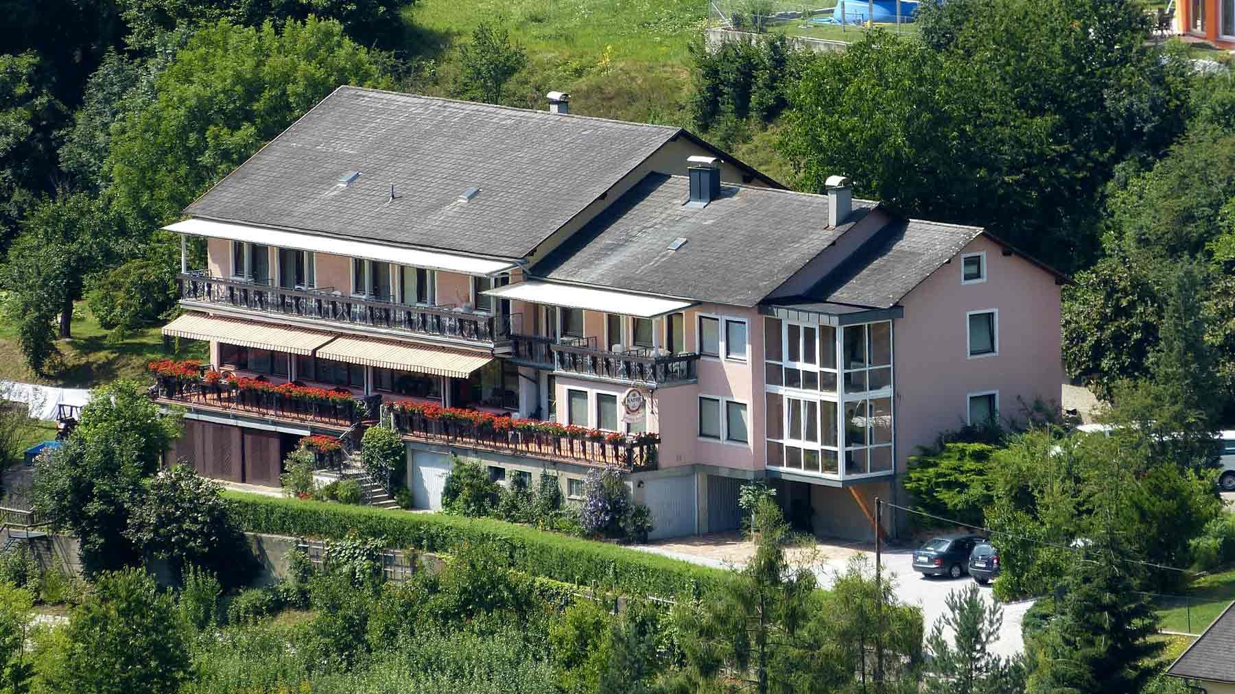 Veľký dom s balkónom a záhradou, obklopený stromami.