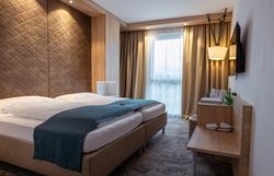 Moderná hotelová izba s manželskou posteľou, dreveným obložením a oknami so závesmi.