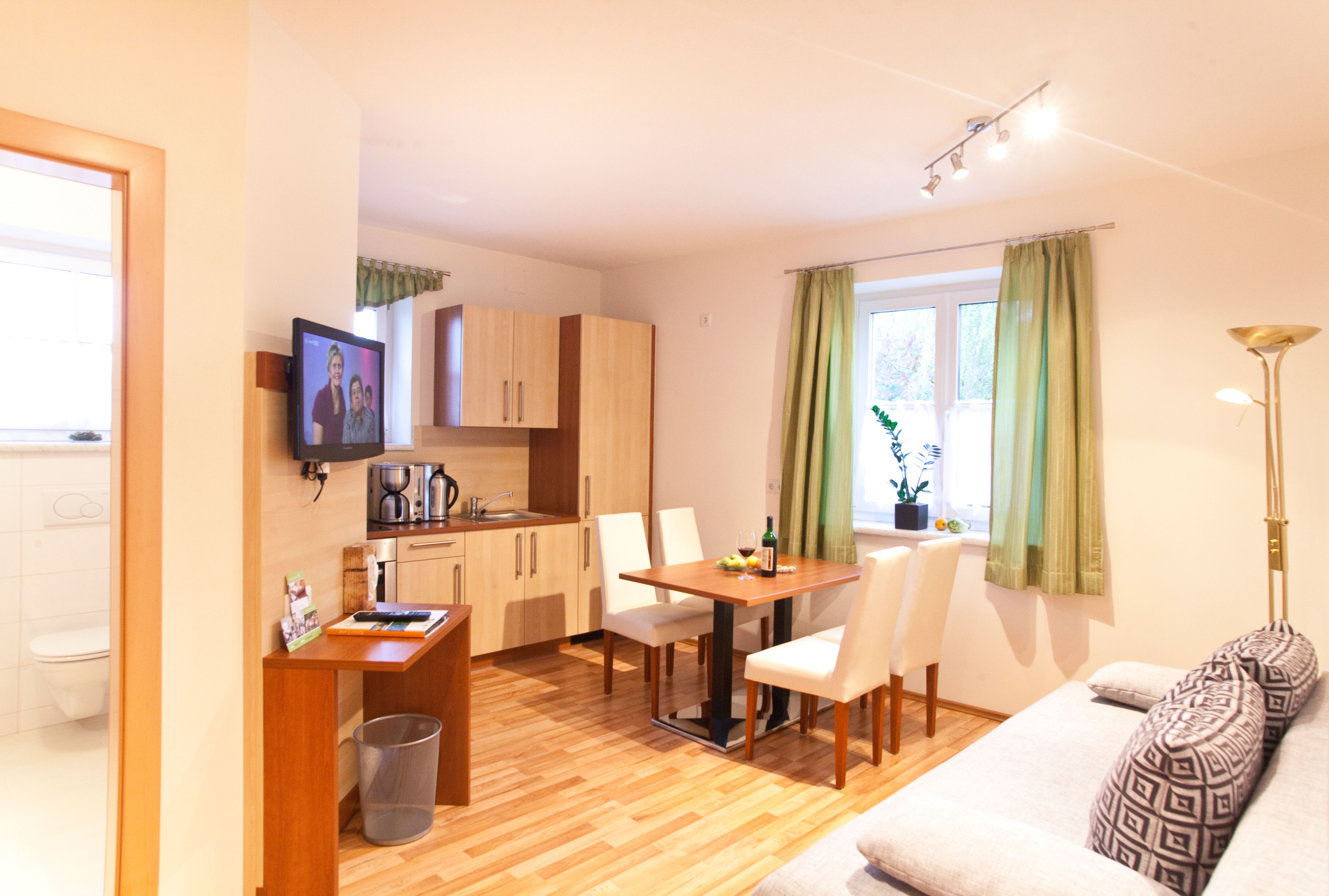 Moderná kuchyňa s jedálenským stolom, pohovkou a TV vo svetlej miestnosti.