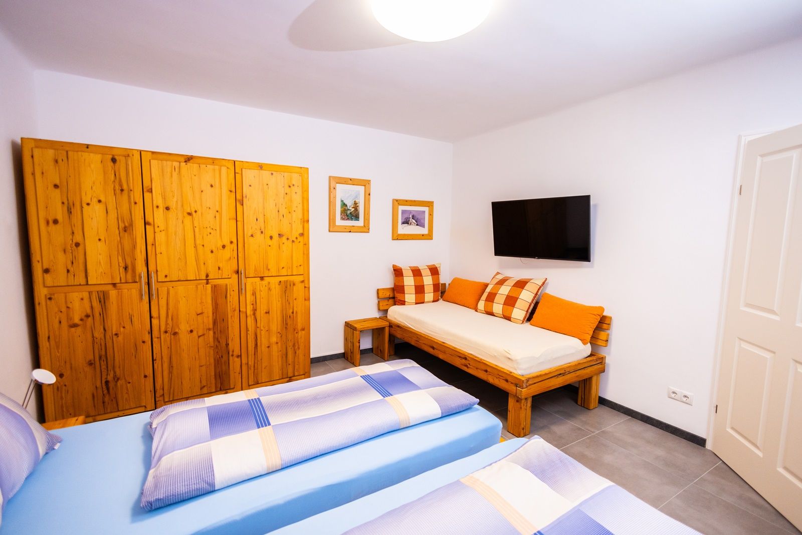 Spálňa s dreveným nábytkom, dvoma posteľami, pohovkou, TV a obrázkami na stene.