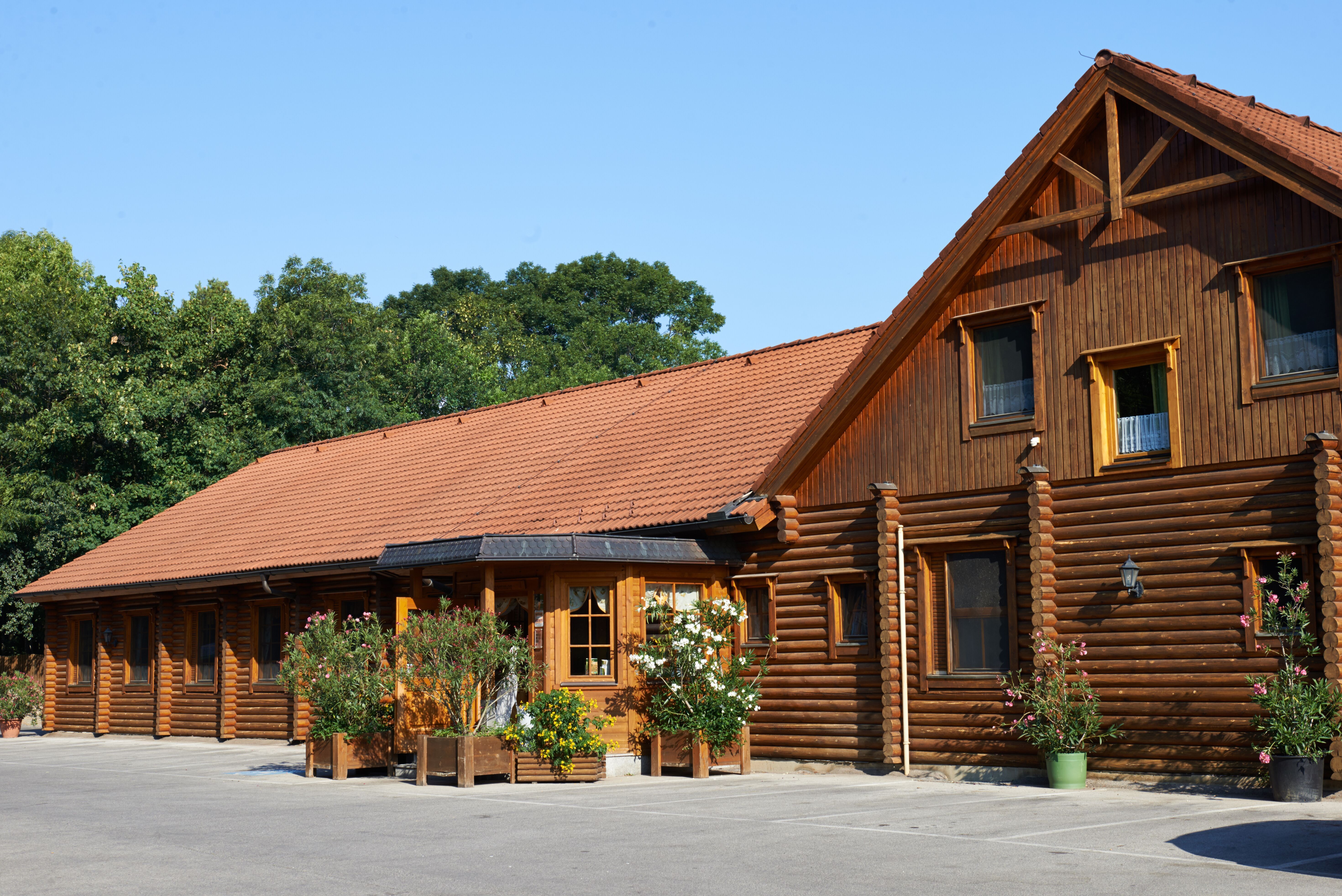 Zrubová chata s červenou škridlovou strechou a rastlinami pred ňou.