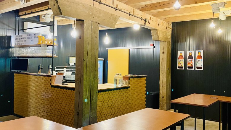 Pohľad do interi&eacute;ru modernej kaviarne s dreven&yacute;mi tr&aacute;mami, barov&yacute;m pultom a vysok&yacute;mi stolmi.