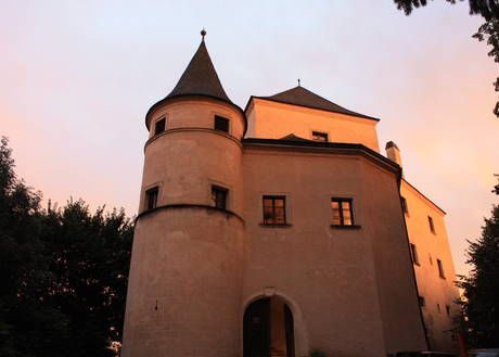 Hrad Wildegg pri západe slnka s osvetlenými vežami a oknami.