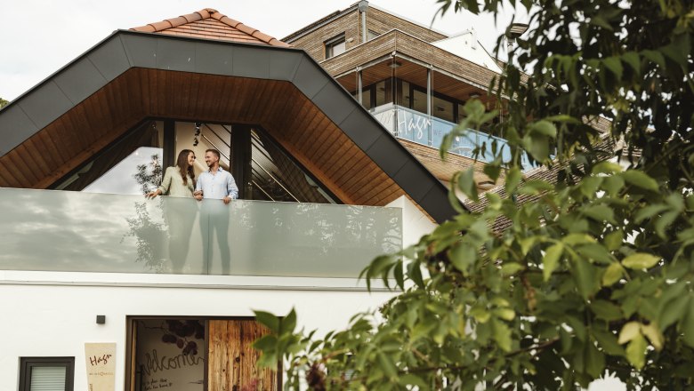 Modern&aacute; budova s p&aacute;rom na balk&oacute;ne, obklopen&aacute; stromami.