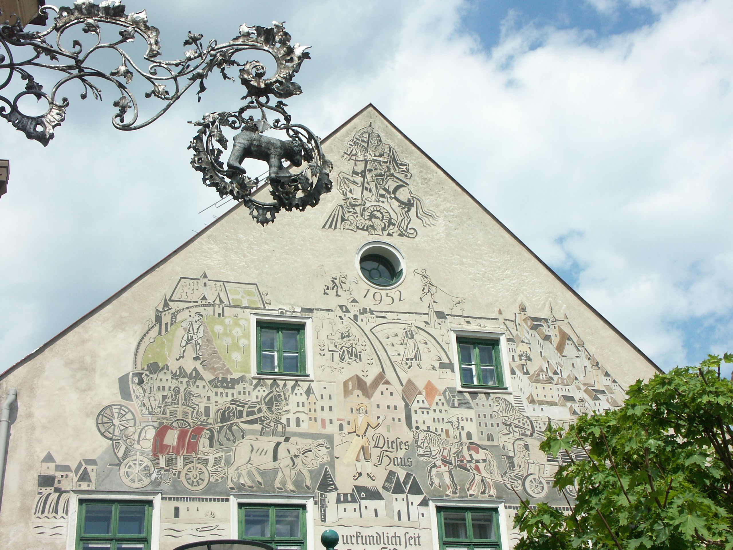 Fasáda domu s umeleckými dielami sgrafita a ozdobným kovovým nápisom.