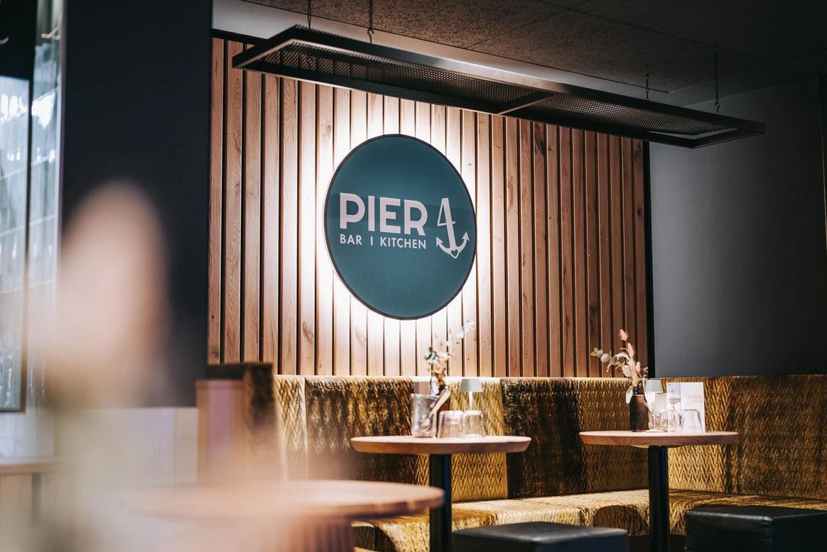 Pohľad do interiéru reštaurácie Pier 4 s drevenou stenou a logom.