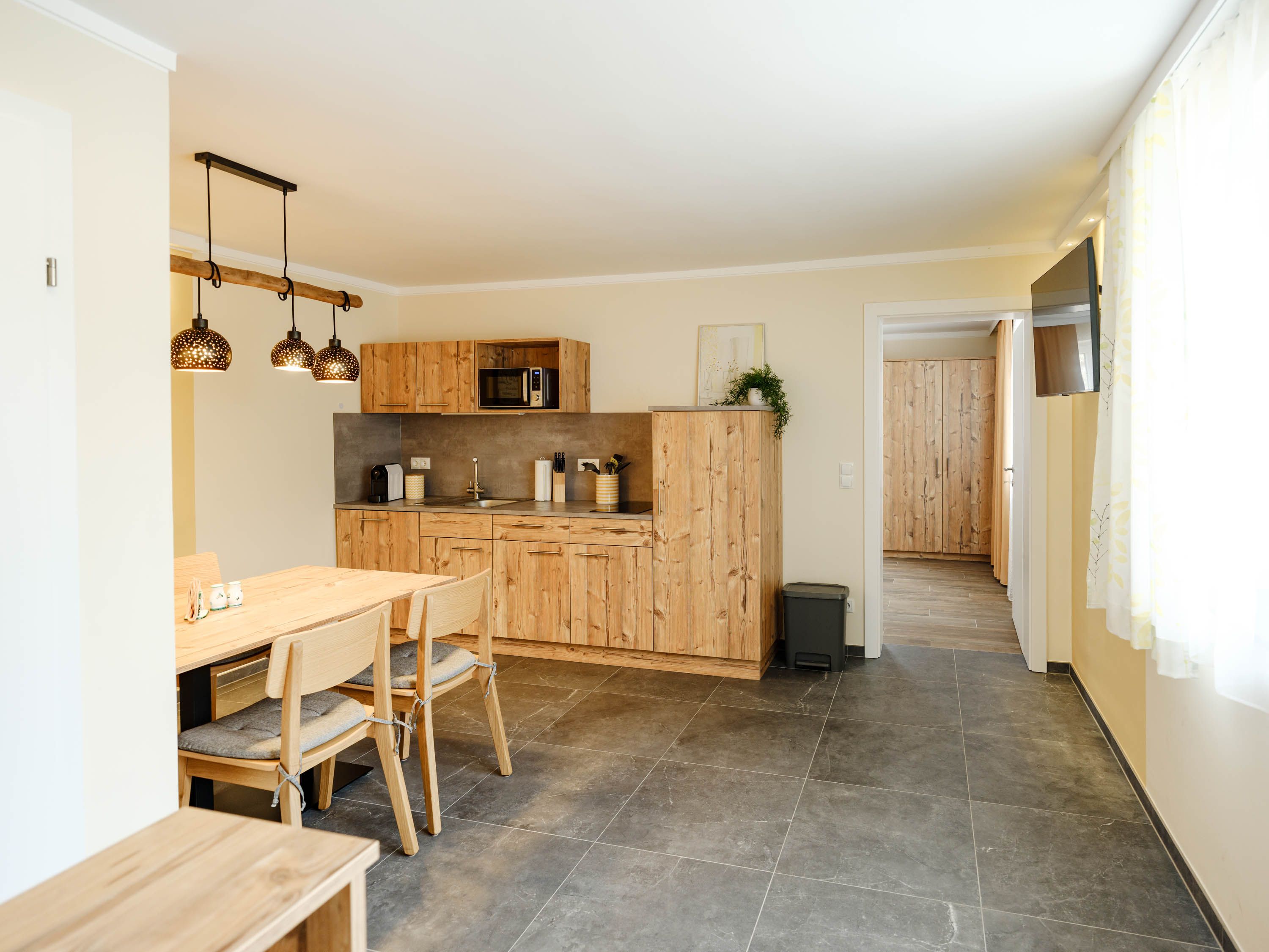 Moderná kuchyňa s dreveným nábytkom a jedálenským stolom, svetlé osvetlenie.