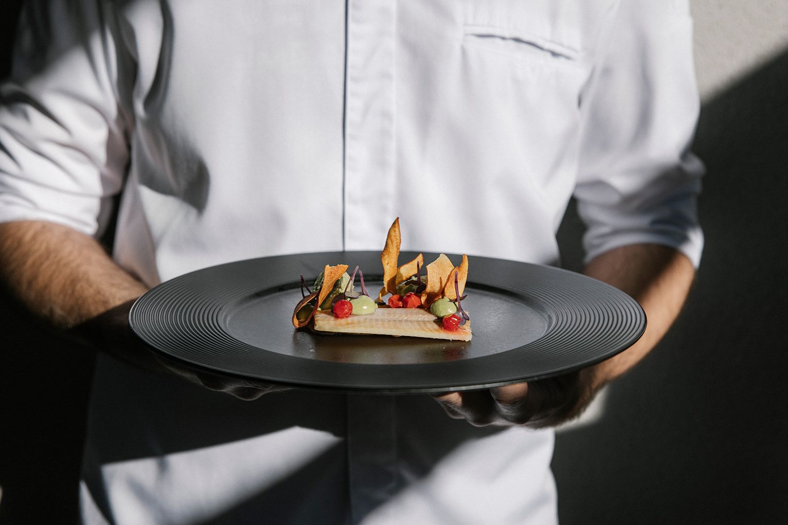 Osoba v bielej košeli drží tanier s dôkladne pripraveným gurmánskym pokrmom.