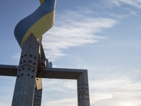 Veľk&aacute; socha v tvare v&yacute;vrtky pred modrou oblohou so z&aacute;padom slnka.