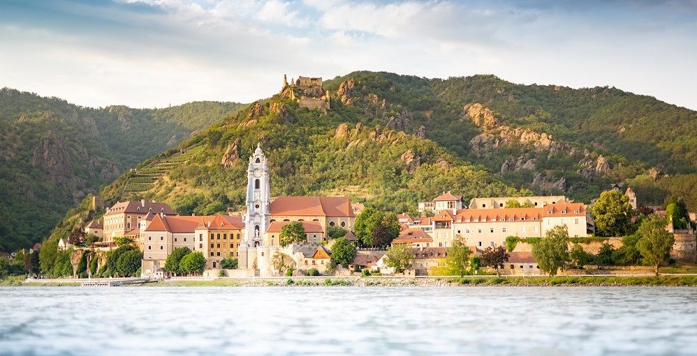 Pohľad na Dürnstein so zrúcaninou kláštora a hradu pred zalesnenými kopcami.