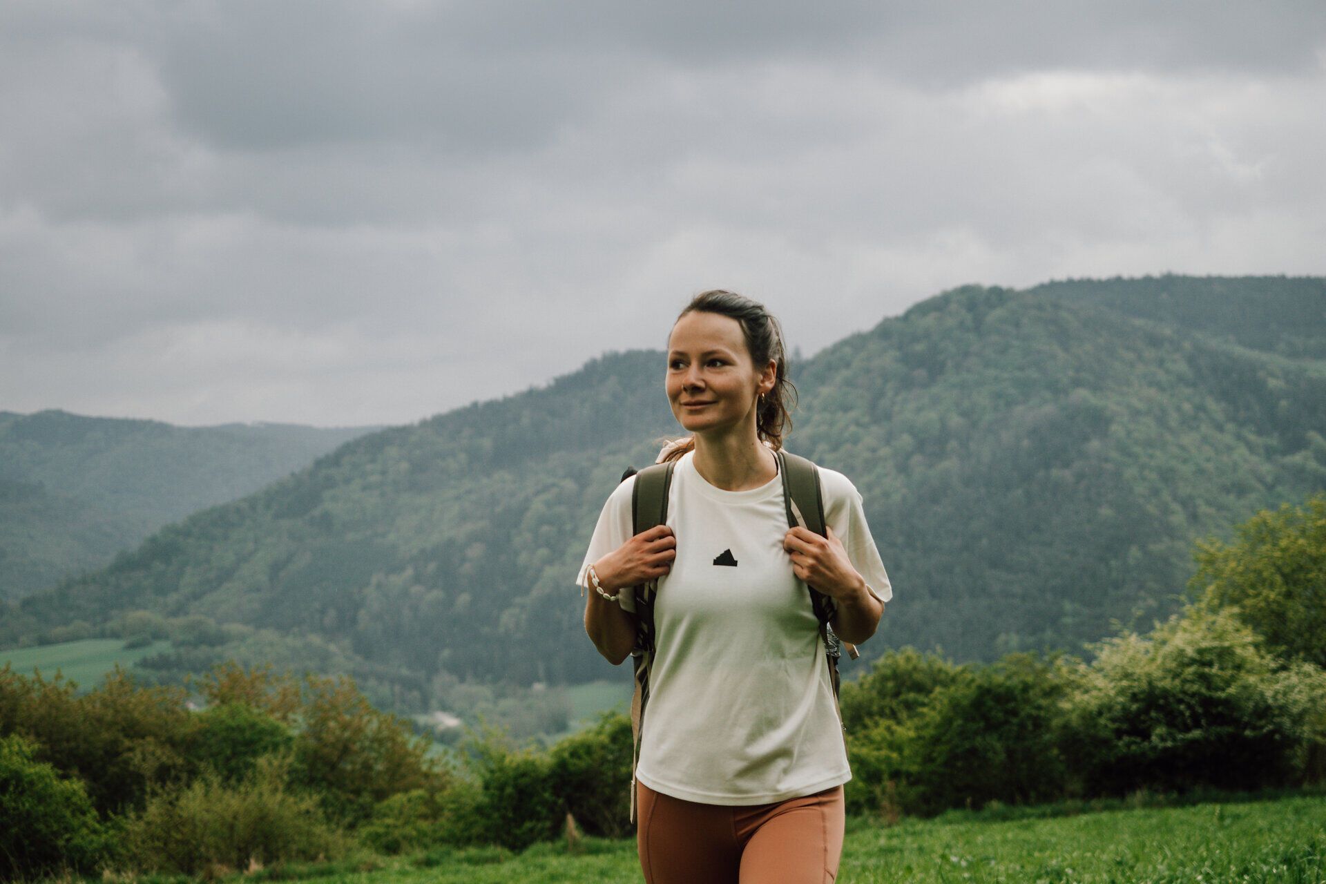 Turista si vychutnáva čerstvý horský vzduch a úchvatný výhľad na kopce a husté lesy. Mraky na oblohe dodávajú scenérii mystickú atmosféru, zatiaľ čo príroda je v plnom rozkvete. Toto idylické prostredie vás pozýva na oddych a objavovanie krás okolia.