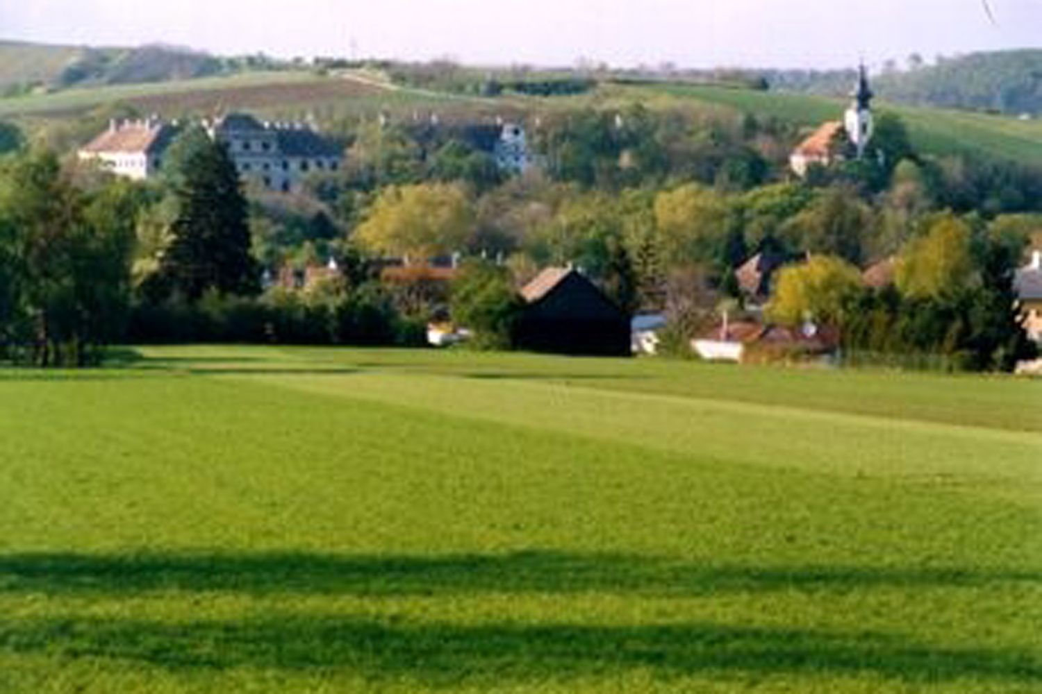 Zelené lúky s dedinou a kostolom v pozadí.
