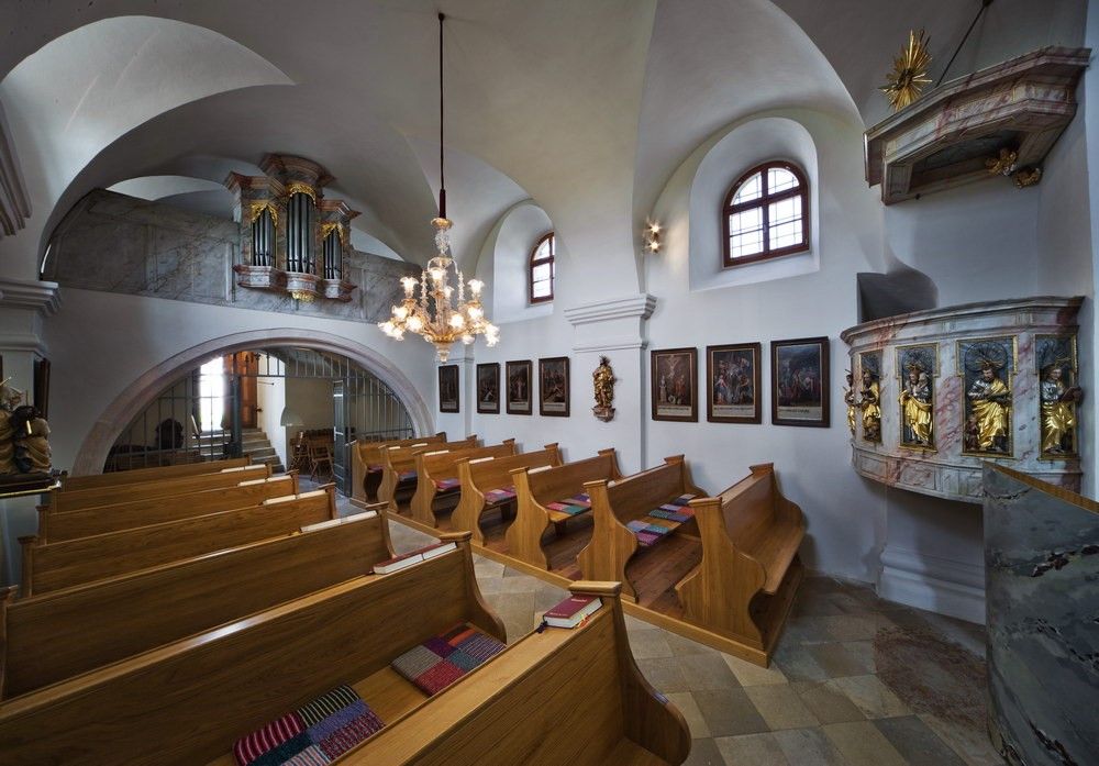 Pohľad do interiéru malého kostola s drevenými lavicami, kazateľnicou a organom na galérii.
