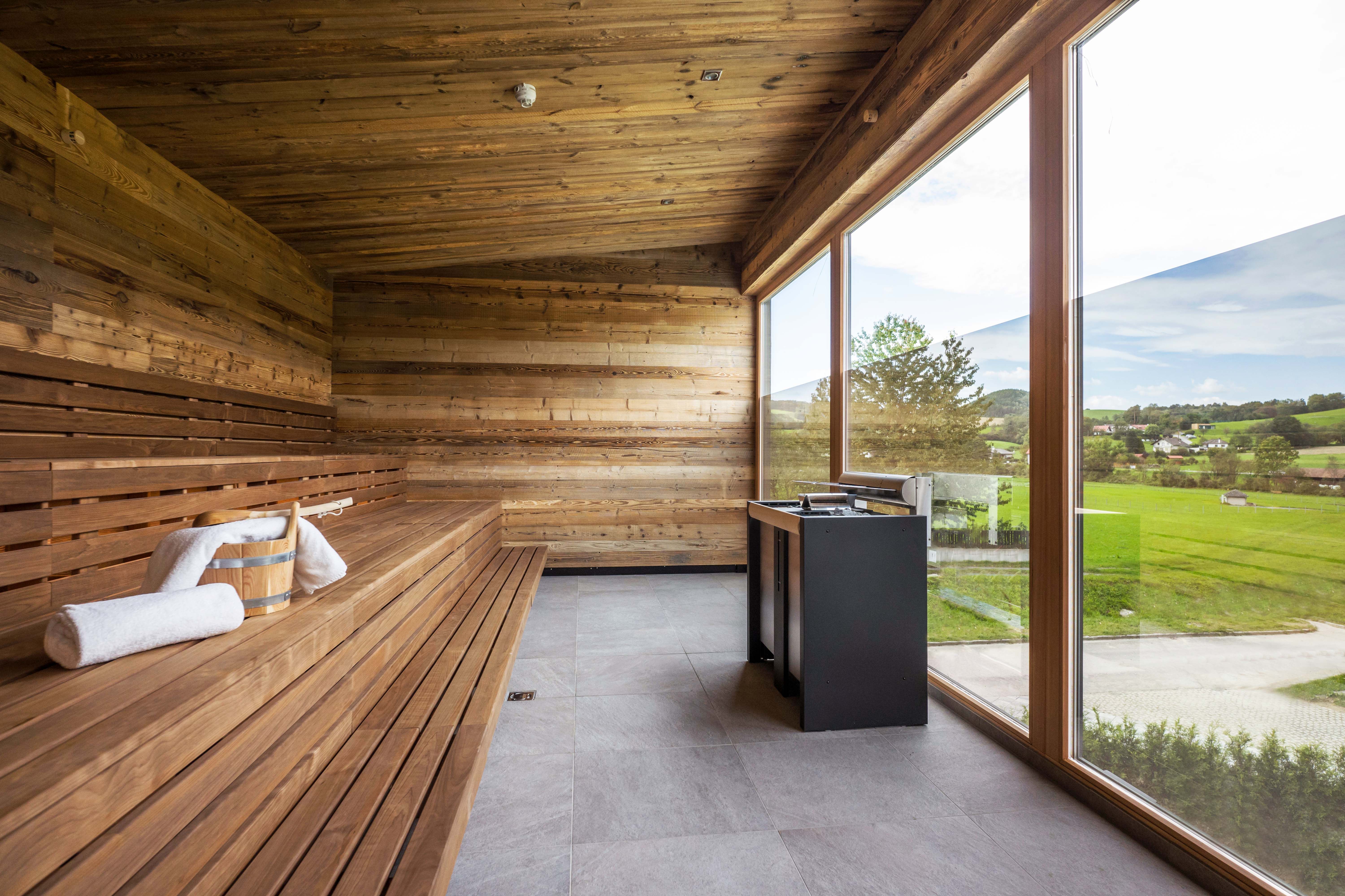 Moderná sauna s dreveným obložením a veľkým preskleným priečelím s výhľadom na zeleň.