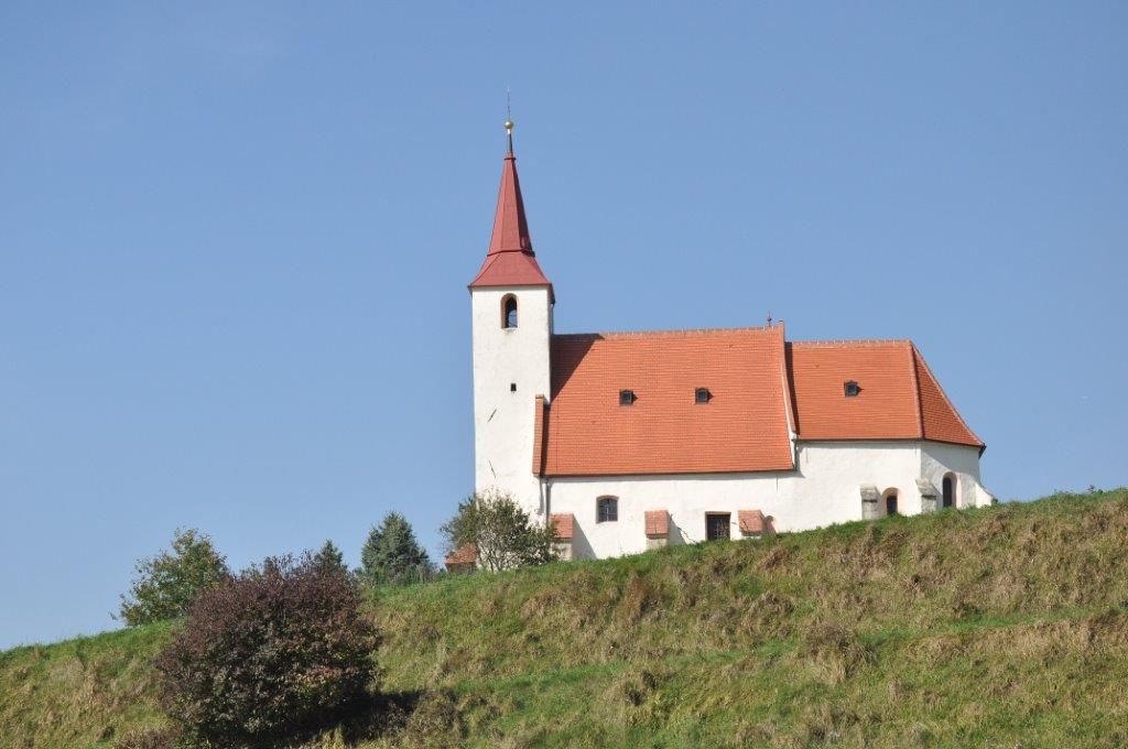 Farský kostol Ofenbach na kopci s modrou oblohou v pozadí.
