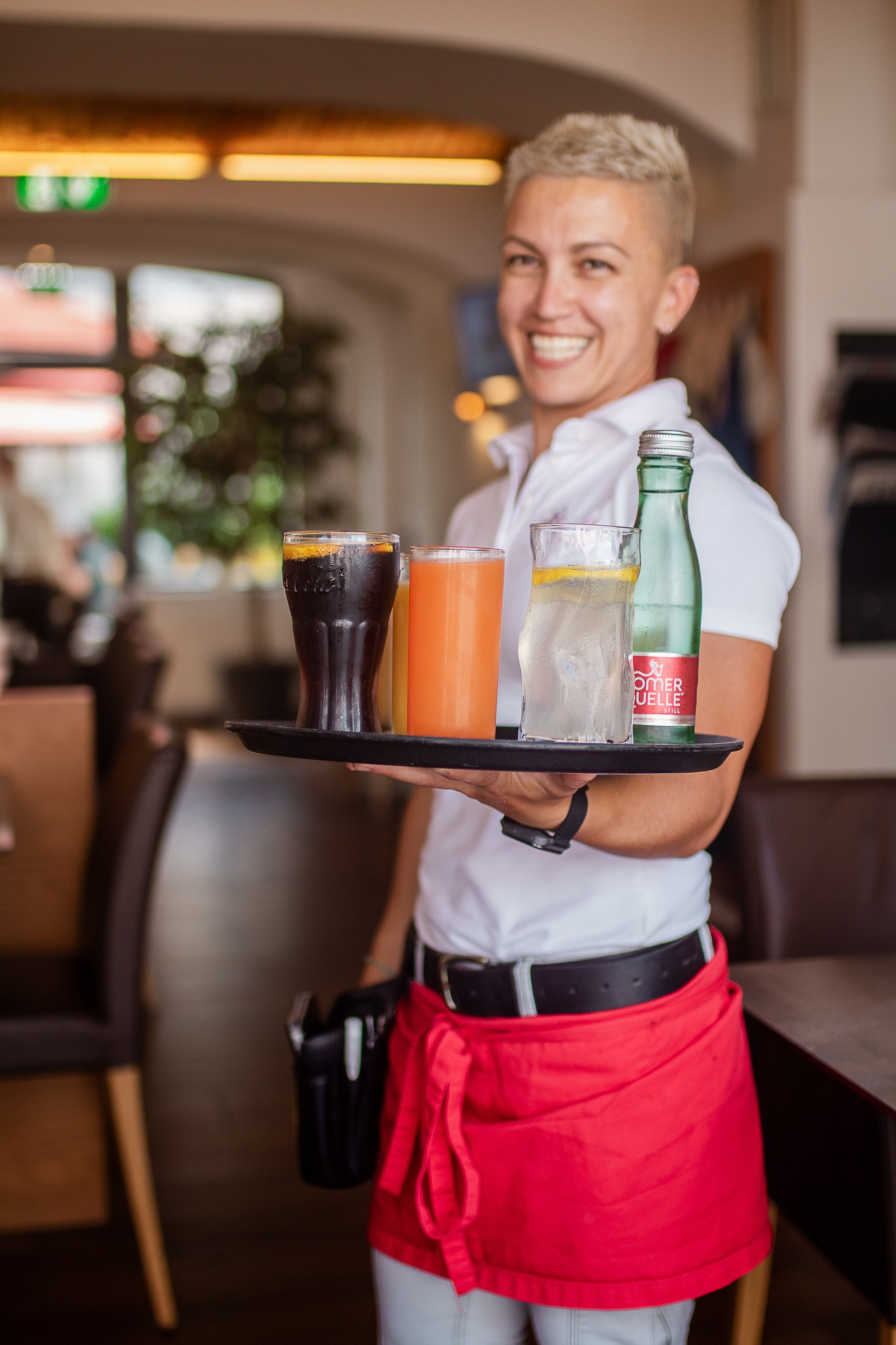Usmievajúca sa čašníčka v reštaurácii nesie podnos s rôznymi nápojmi.