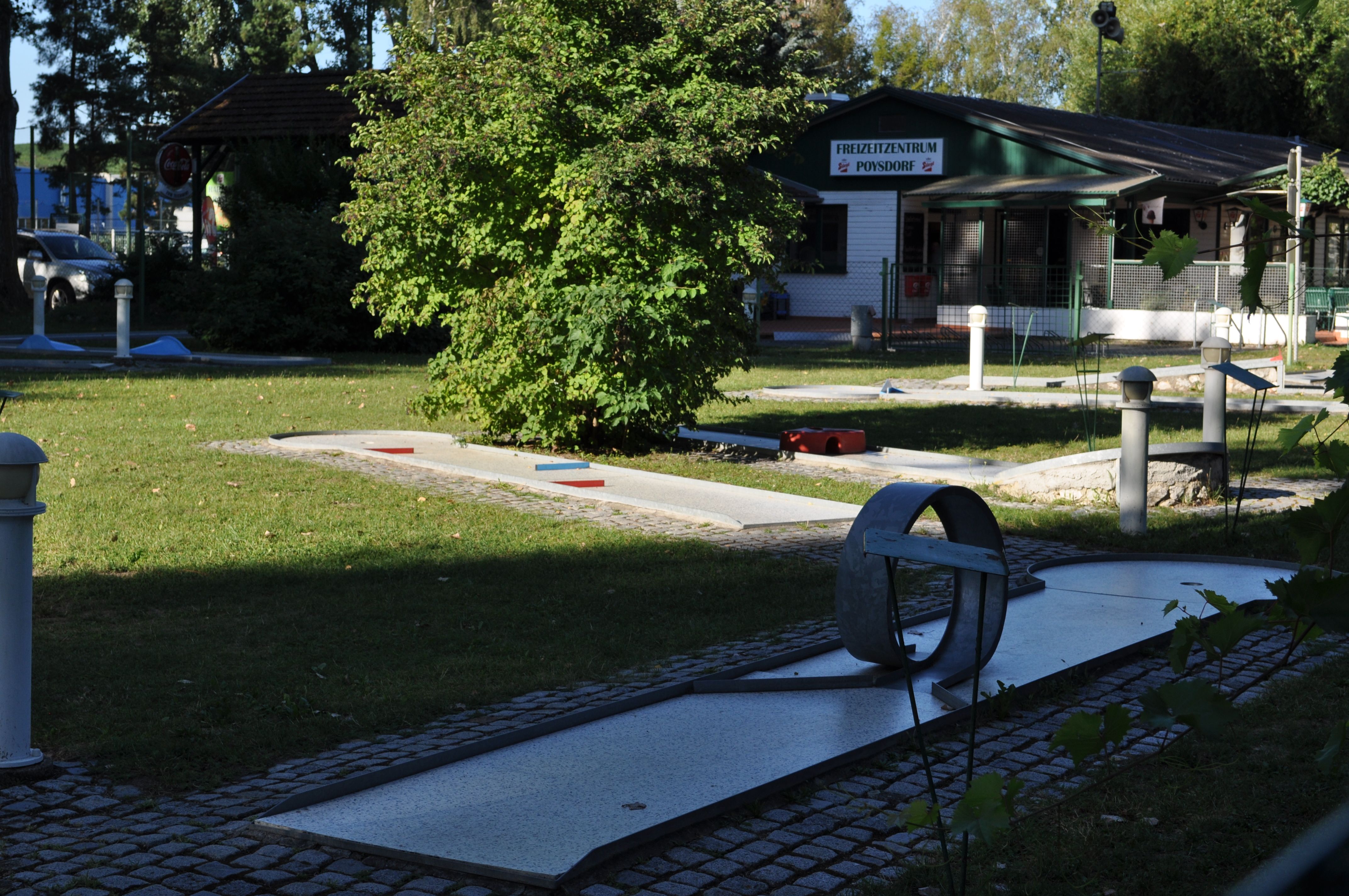 Minigolfové ihrisko s prekážkami a budovou v pozadí.