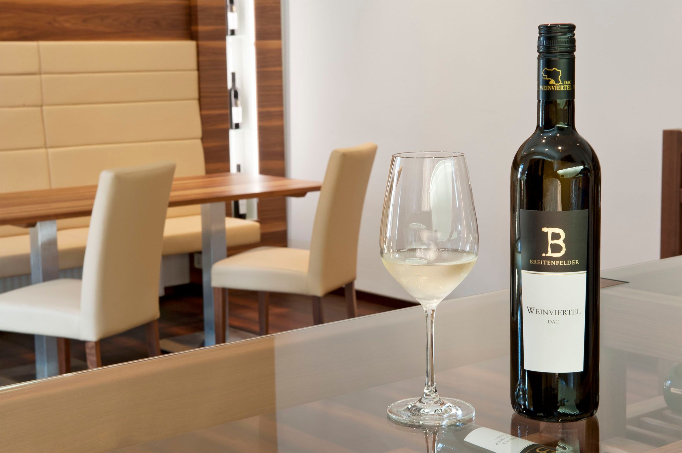Degustačná miestnosť s fľašou bieleho vína a naplneným pohárom na stole.