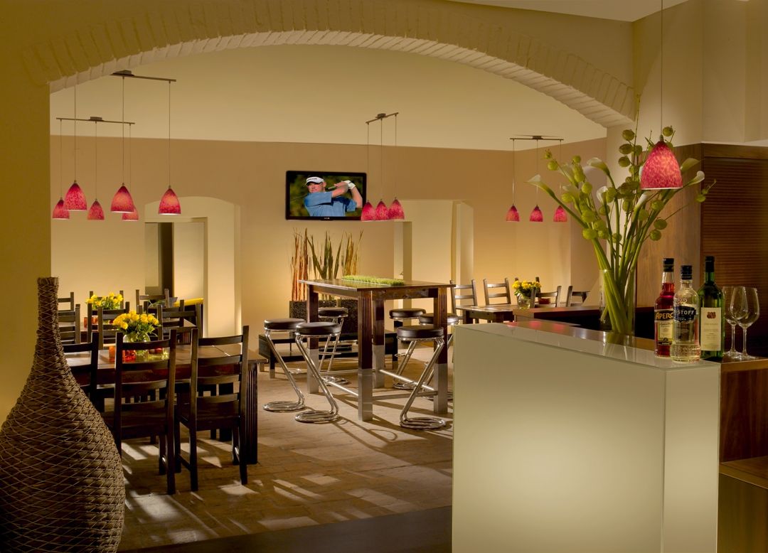 Pohľad do interiéru štýlovej reštaurácie s moderným nábytkom a červenými závesnými lampami.