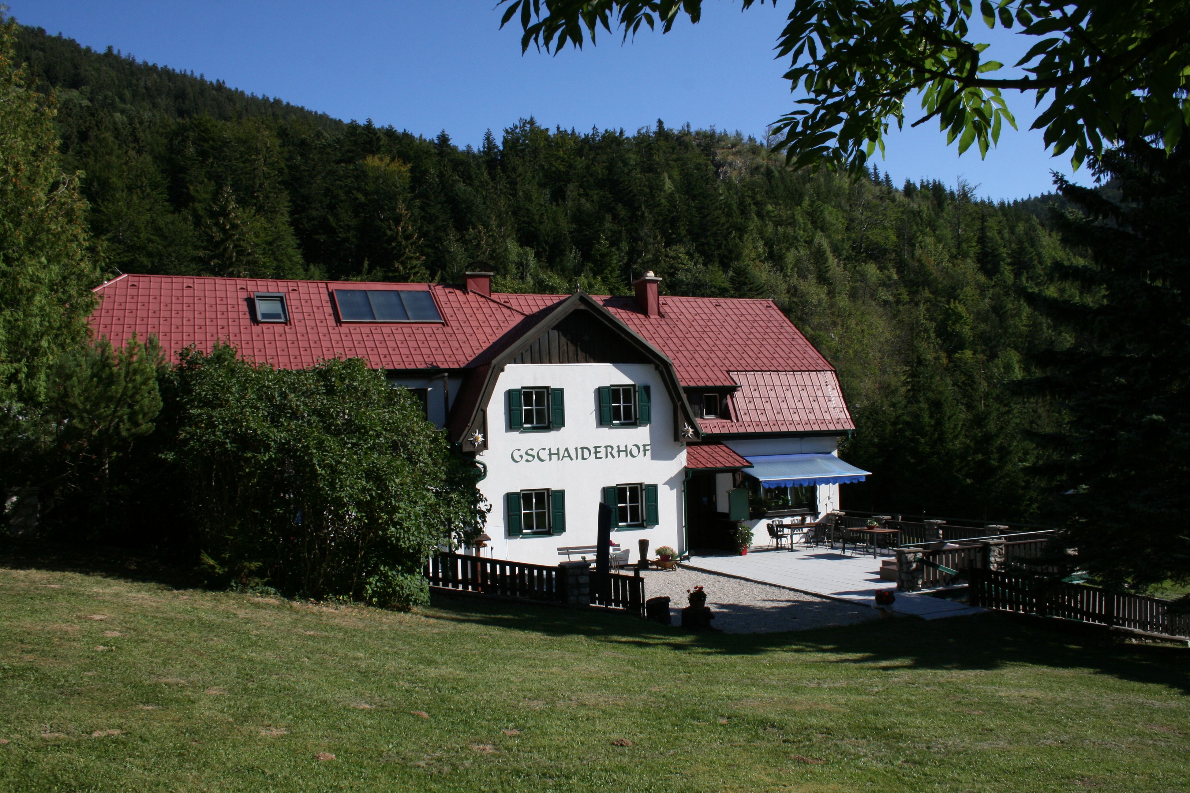 Tradičný dom s červenou strechou, obklopený lesmi a lúkami, s označením "Gschaiderhof".
