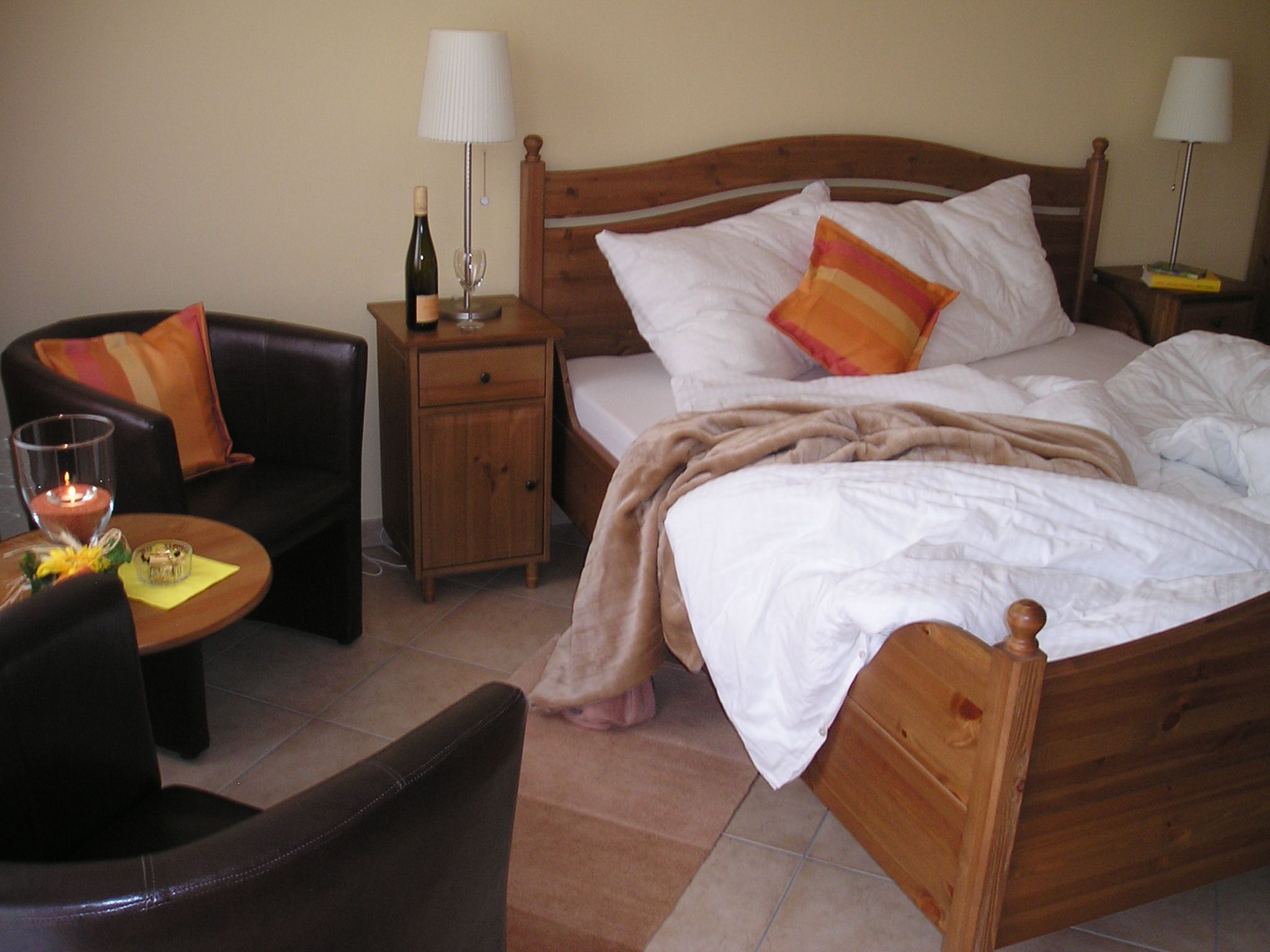 Útulná izba pre hostí s manželskou posteľou, nočným stolíkom, lampou, kreslom a stolom.