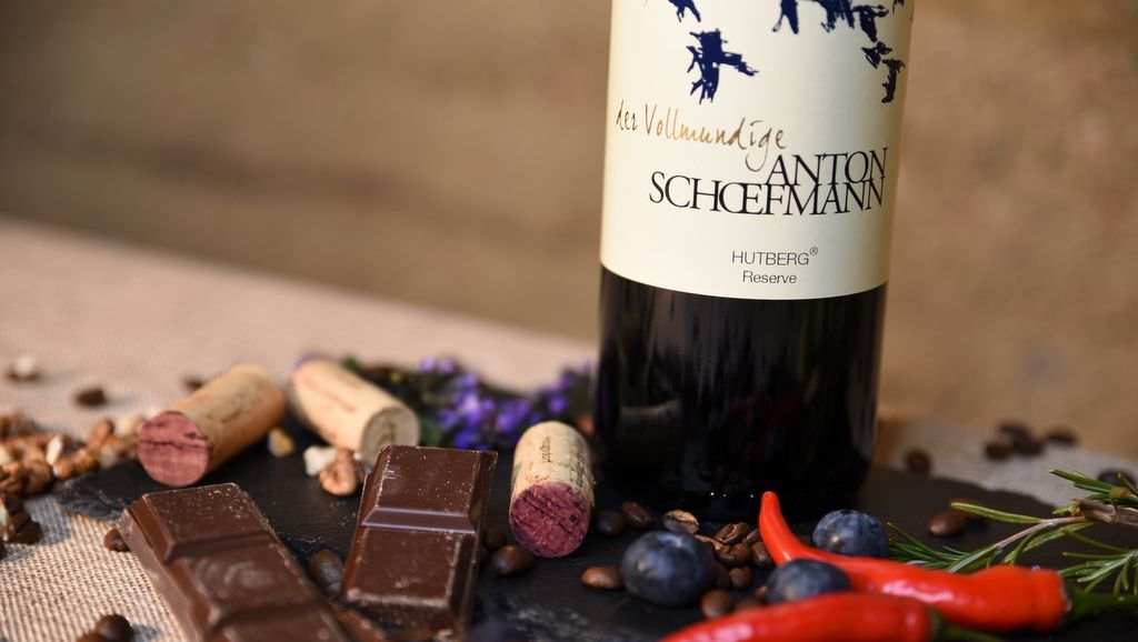 Fľaša vína s čokoládou, korkom a korením na stole.