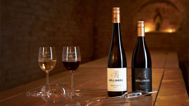 Dva poh&aacute;re na v&iacute;no a dve fľa&scaron;e v&iacute;na na drevenom stole vo v&iacute;nnej pivnici.