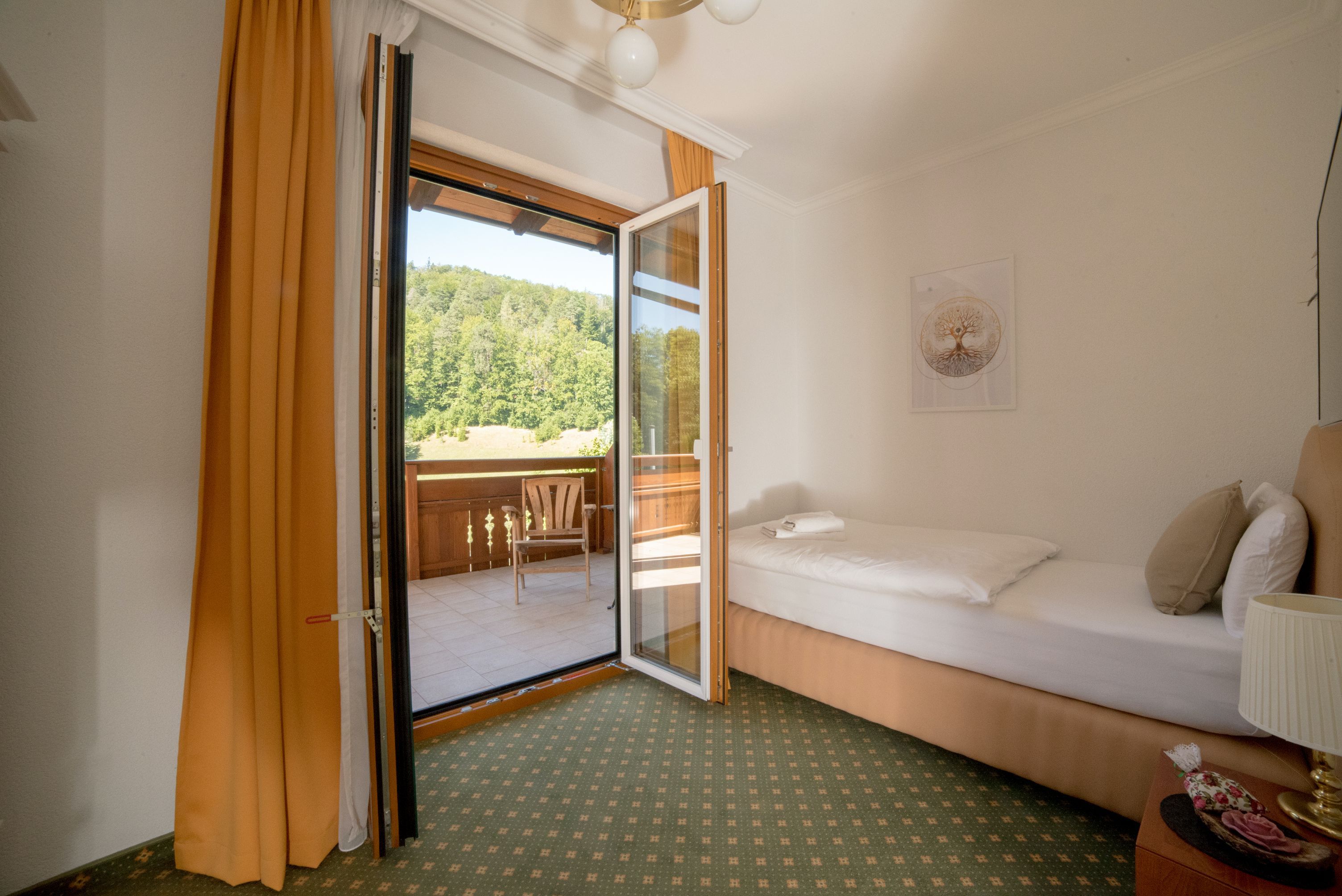 Jednolôžková izba s balkónom, samostatné lôžko, otvorené balkónové dvere, výhľad na zelenú krajinu.