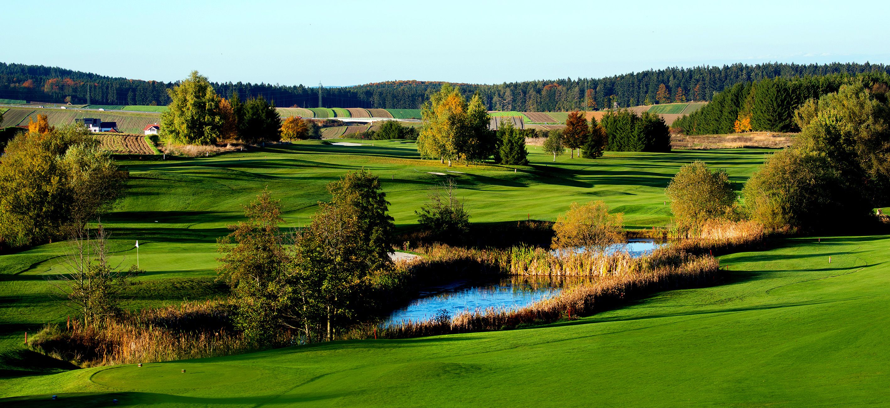 Zelená krajina golfového ihriska s rybníkom a stromami na jeseň.