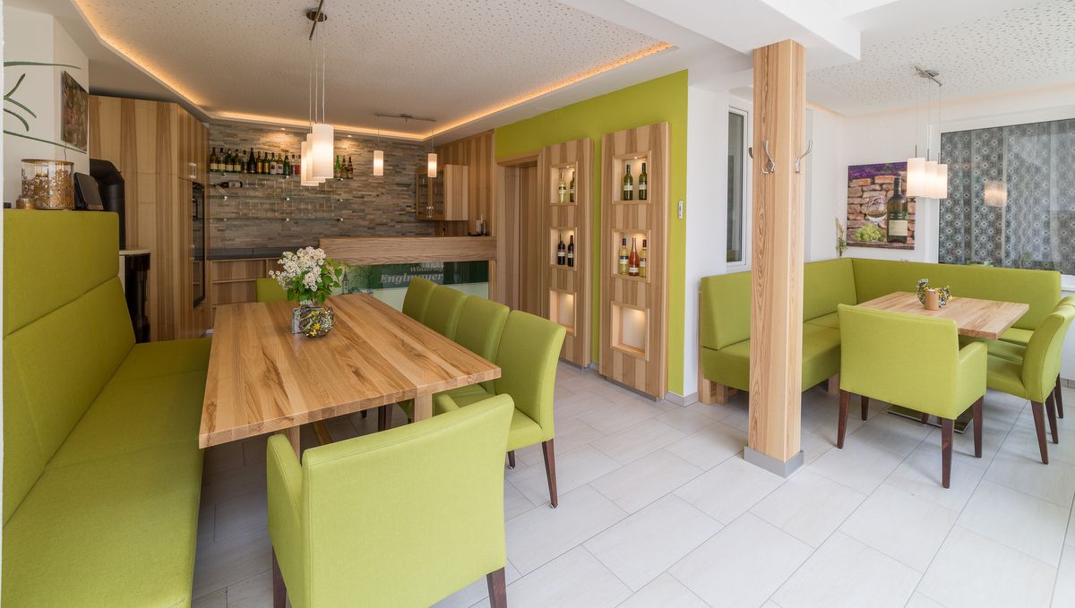 Moderná degustačná miestnosť s drevenými stolmi a zeleným čalúneným nábytkom.