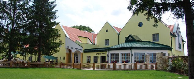 Žltá budova s hotelom a reštauráciou, obklopená stromami a trávnikom.