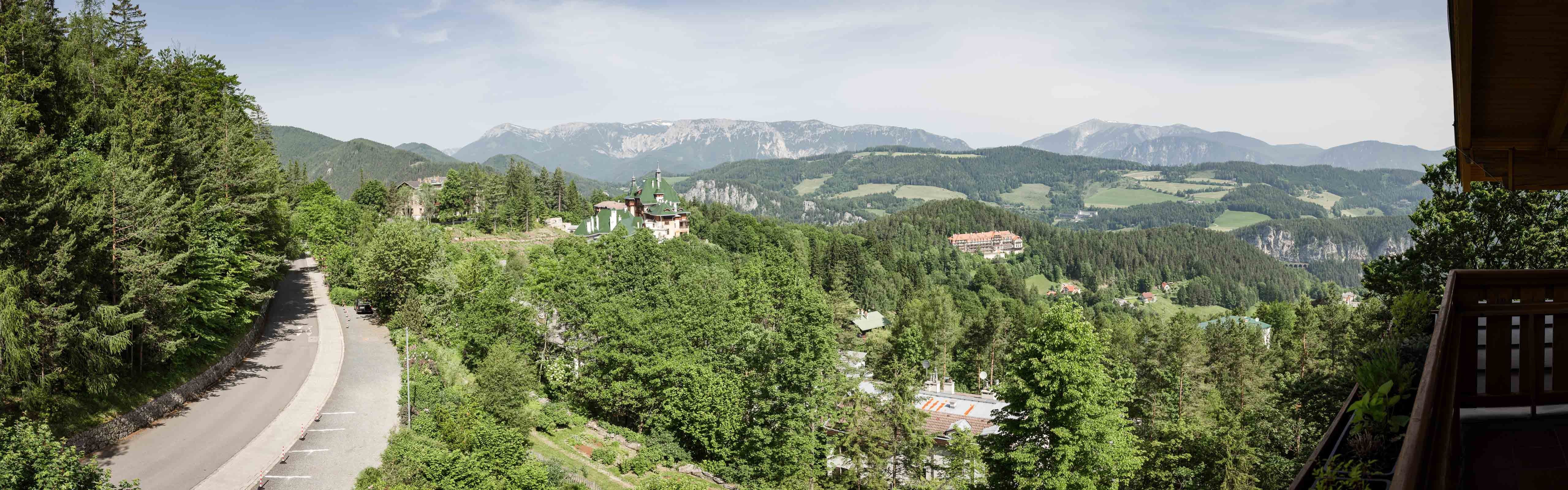 Panoramatický pohľad na hornatú krajinu s lesom, cestou a budovami.
