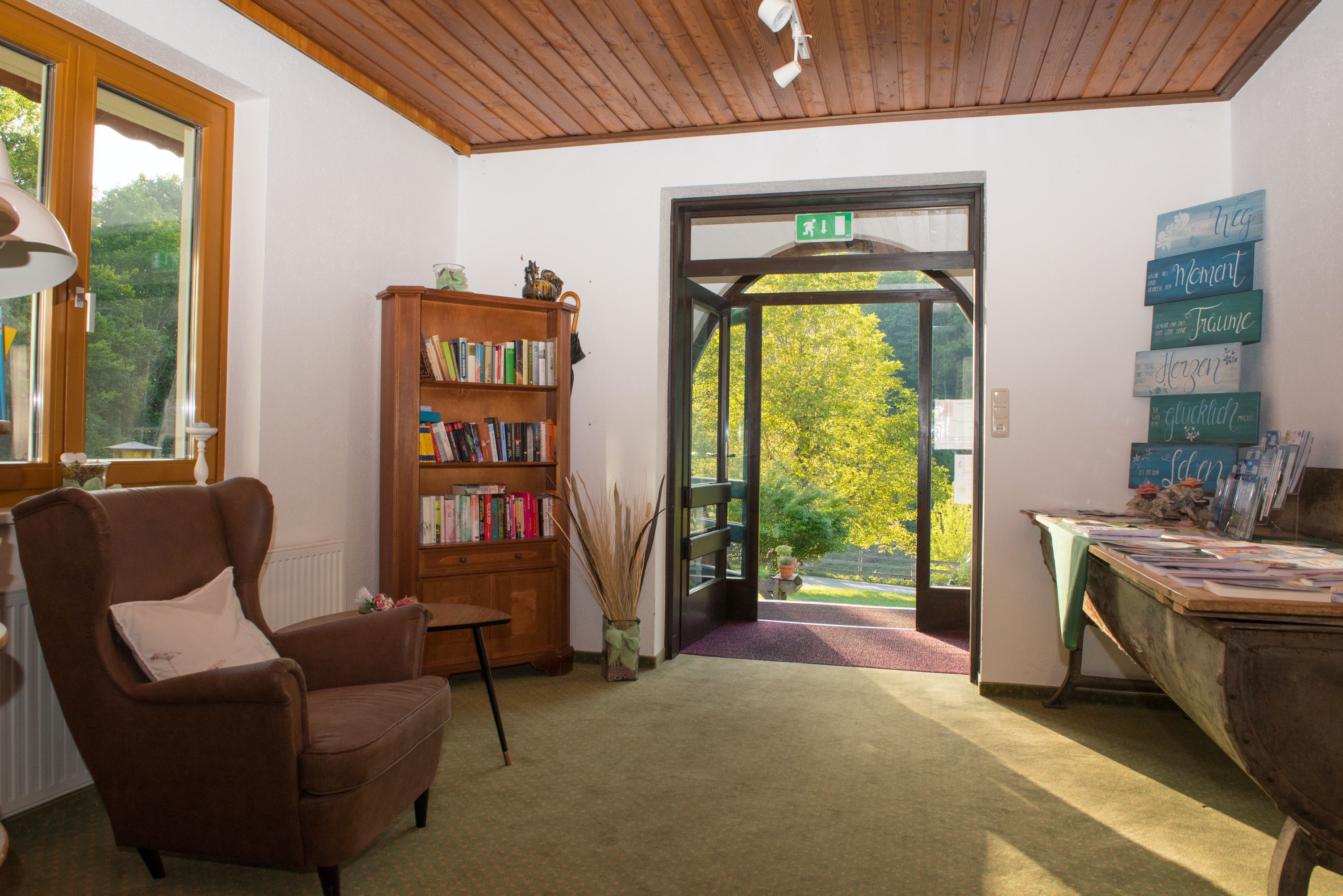 Vstupný priestor s kreslom, policou na knihy a otvorenými dverami s výhľadom na zeleň.