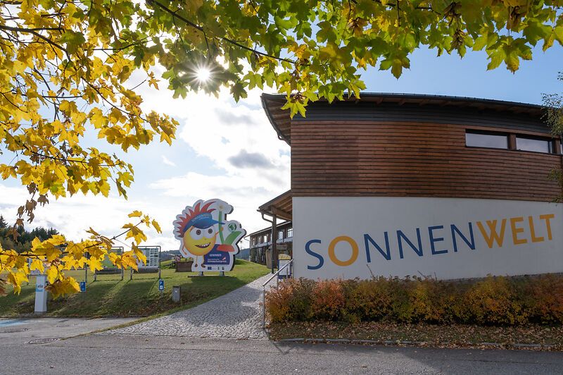 Vchod do SONNENWELT Großschönau s jesennými stromami a slnkom.