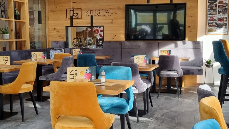 Pohľad do interi&eacute;ru modernej kaviarne s farebn&yacute;mi zamatov&yacute;mi stoličkami a dreven&yacute;mi stenami.