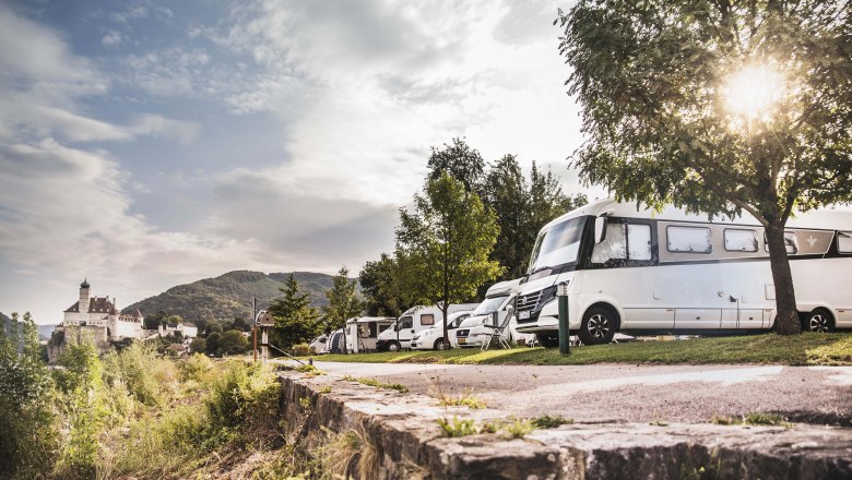 Obytn&eacute; automobily v kempe s hradom v pozad&iacute;.