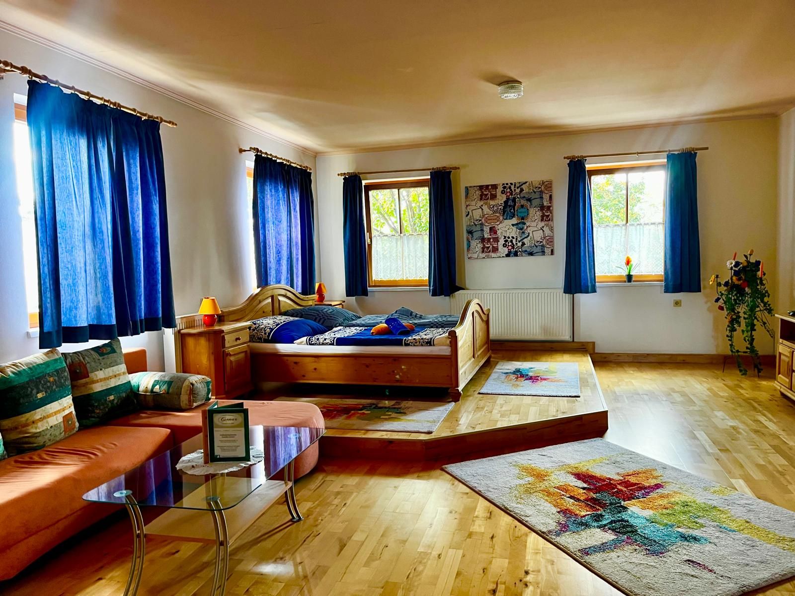 Útulná izba s drevenou podlahou, manželskou posteľou, pohovkou a modrými závesmi.