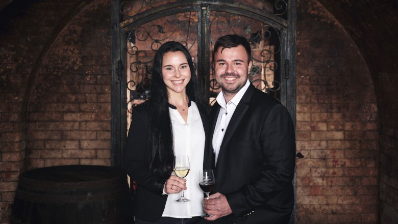 Muž a žena v elegantnom oblečen&iacute; držia poh&aacute;re na v&iacute;no vo v&iacute;nnej pivnici.