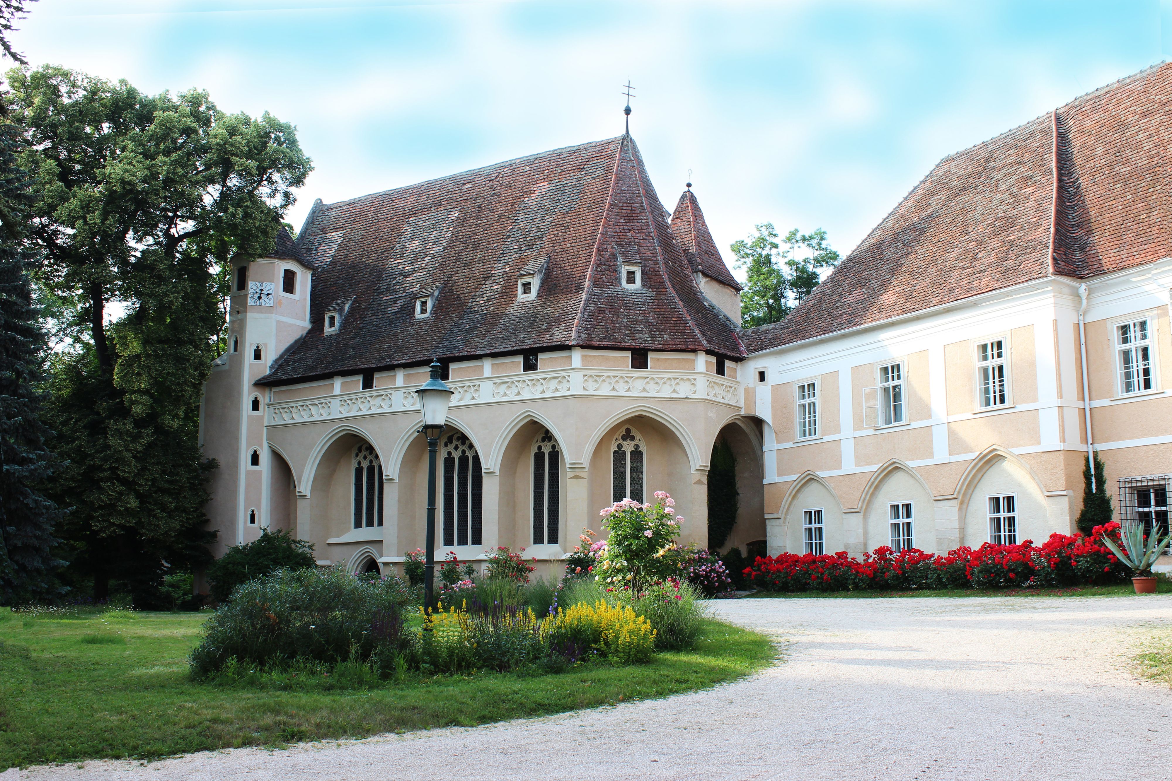 Historická budova so špicatou strechou a záhradou v popredí.