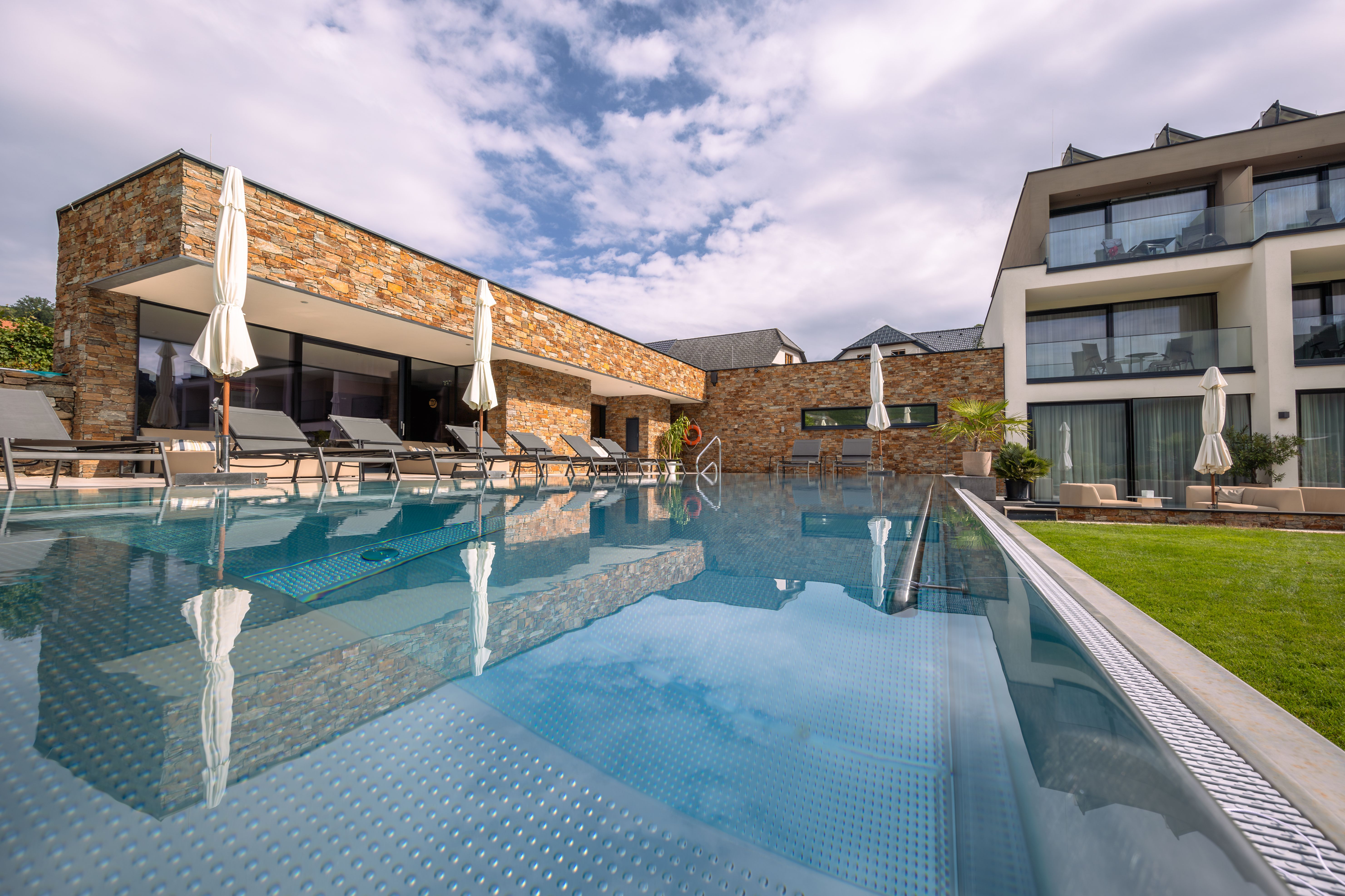 Exteriérový pohľad na moderný hotel s bazénom a ležadlami.