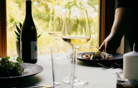 Položený stôl s fľašou vína, pohármi a tanierom s jedlom v reštaurácii.