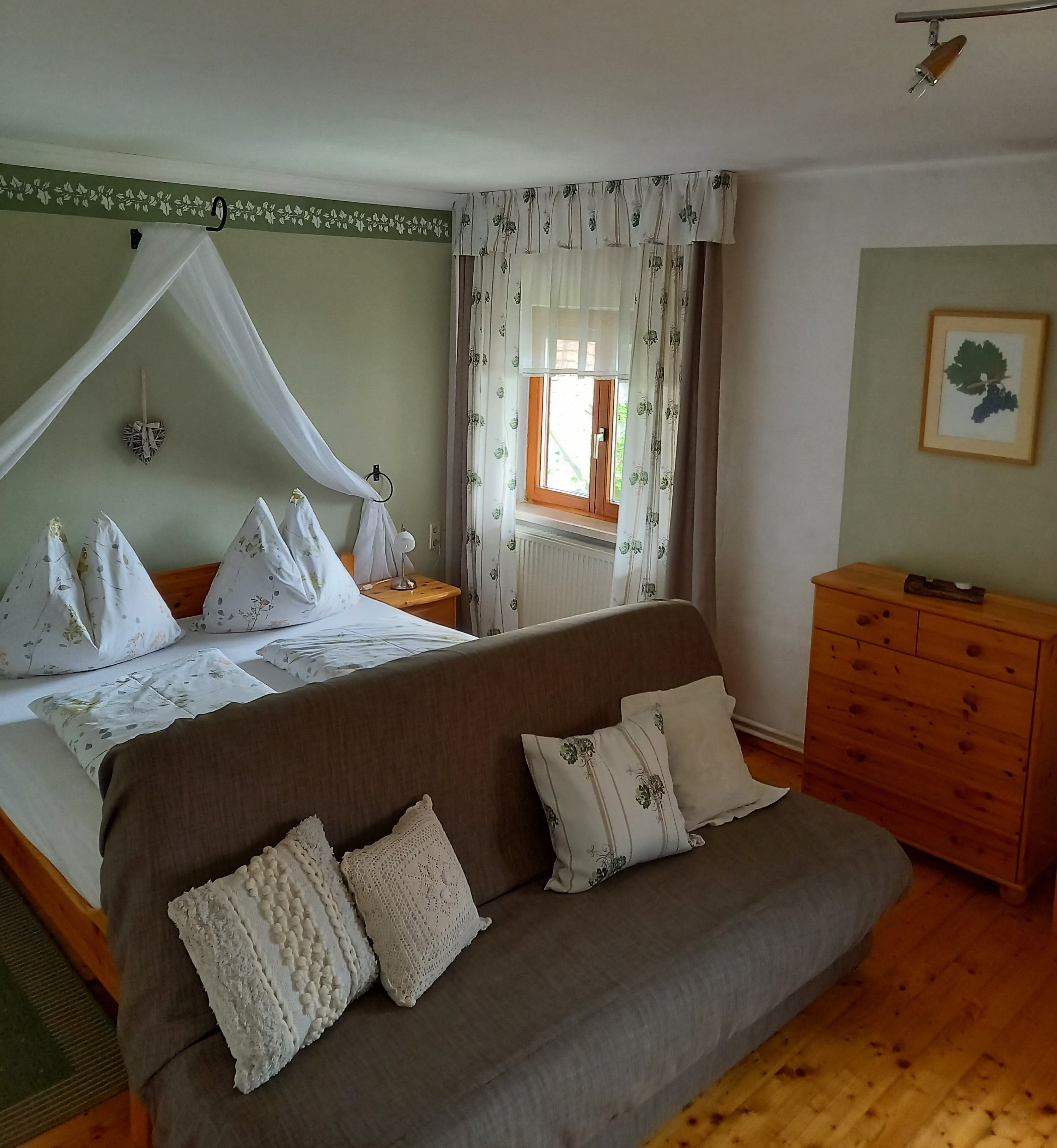 Útulná izba pre hostí s manželskou posteľou, pohovkou a dreveným nábytkom.