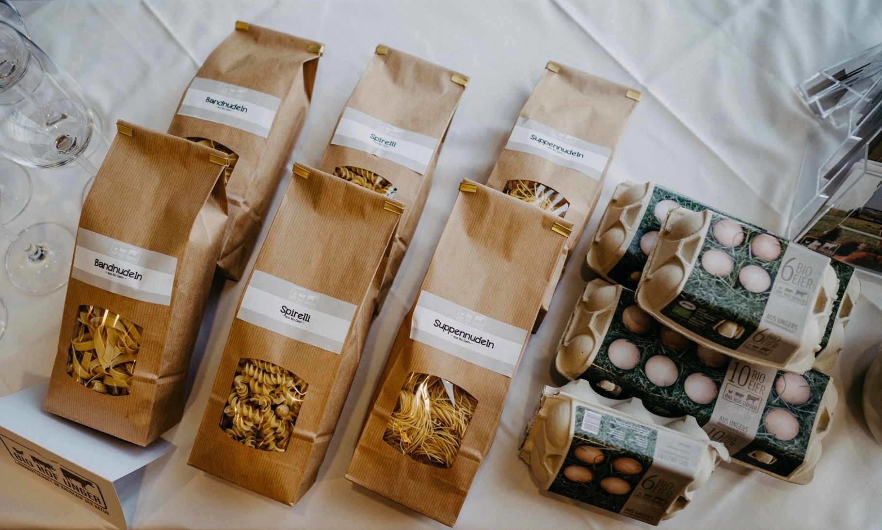 Výrobky spoločnosti Biohof Unger: cestoviny v hnedých vreckách a škatule od vajec na stole.