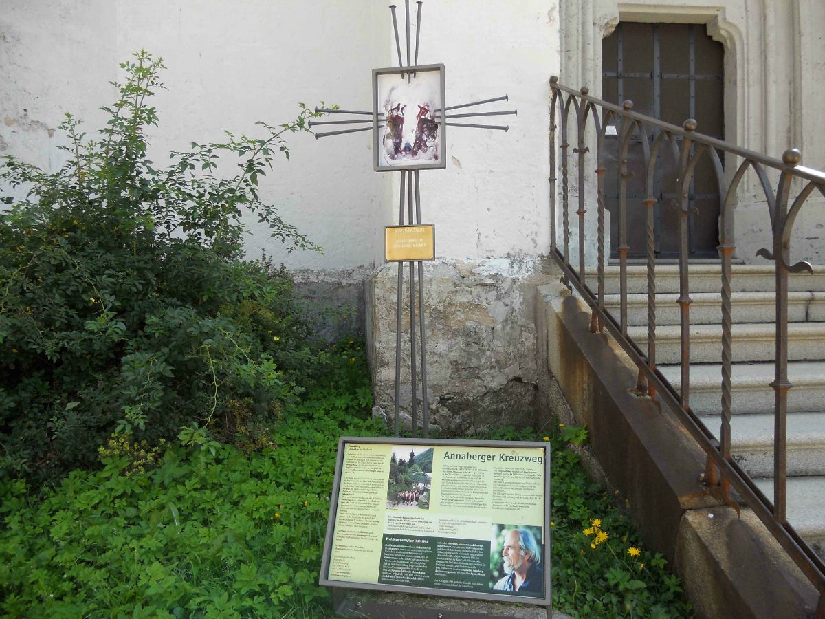 Tabuľa s informáciami o krížovej ceste v Annabergu vedľa schodiska a rastlín.
