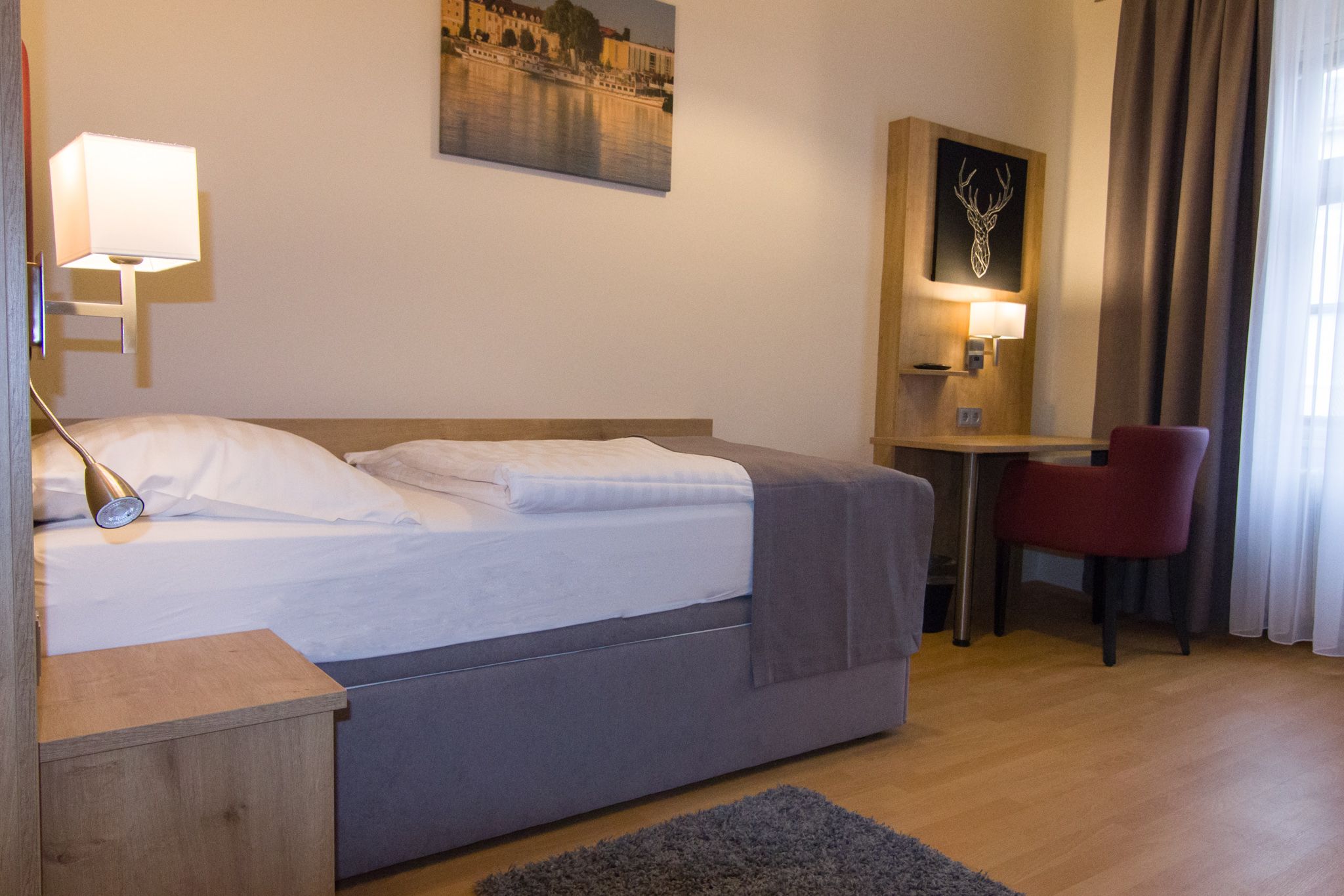 Jednolôžková izba s posteľou, písacím stolom a červenou stoličkou.