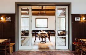 Útulná reštaurácia s dreveným nábytkom a veľkými oknami.